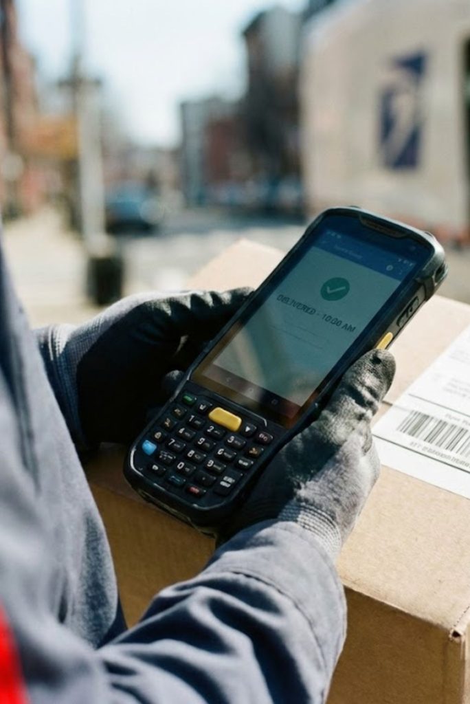 Trabajador con guantes usa un dispositivo móvil para confirmar la entrega de un paquete.